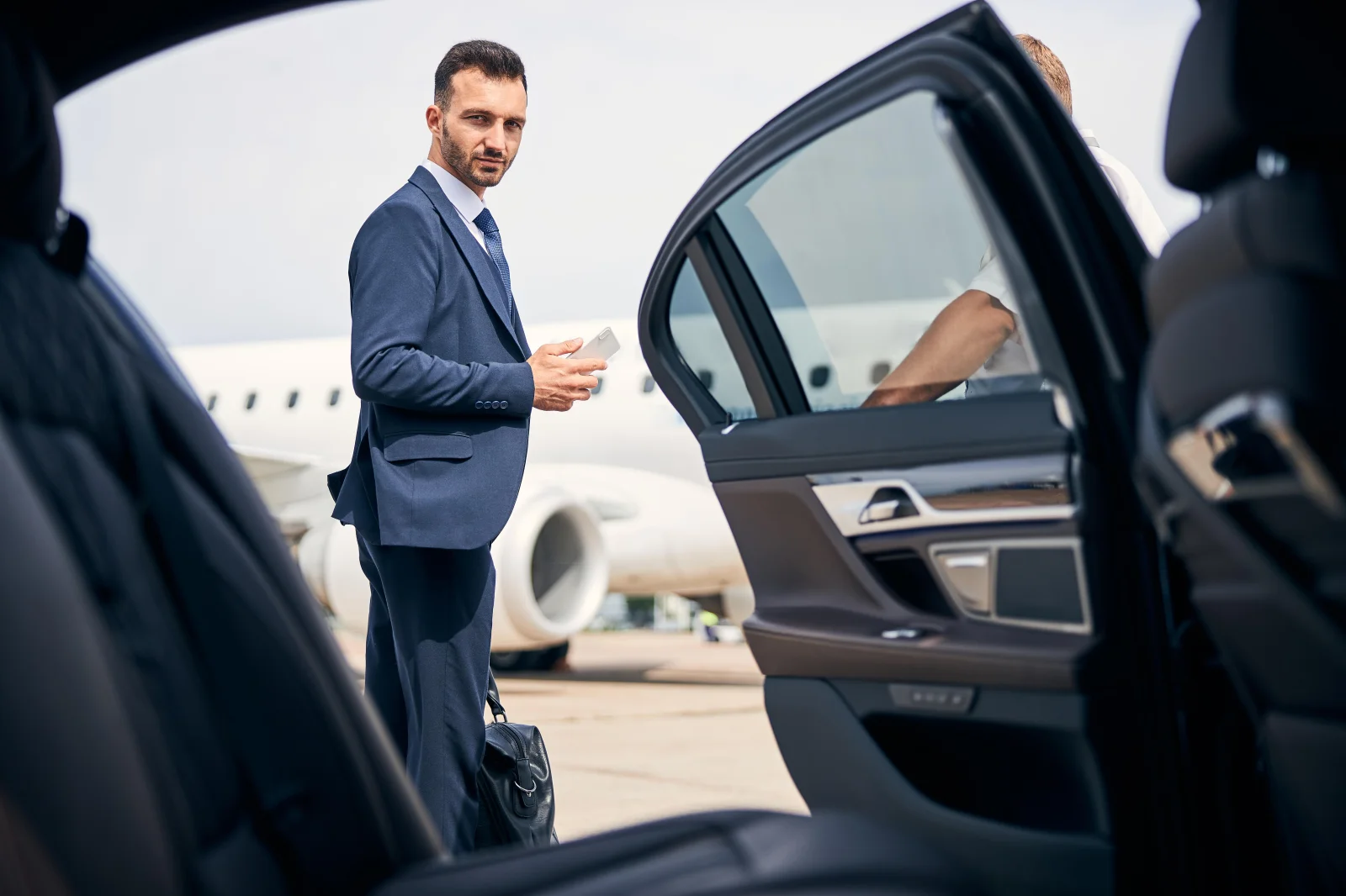 Chauffeur opening the door of a black executive car on a private jet apron